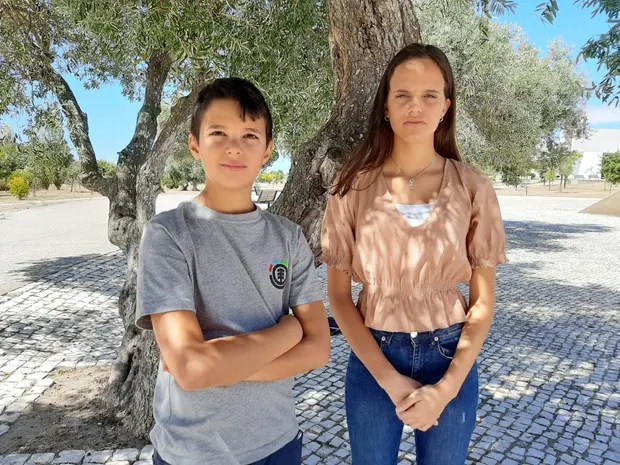 Two youths stand in front of a tree. 