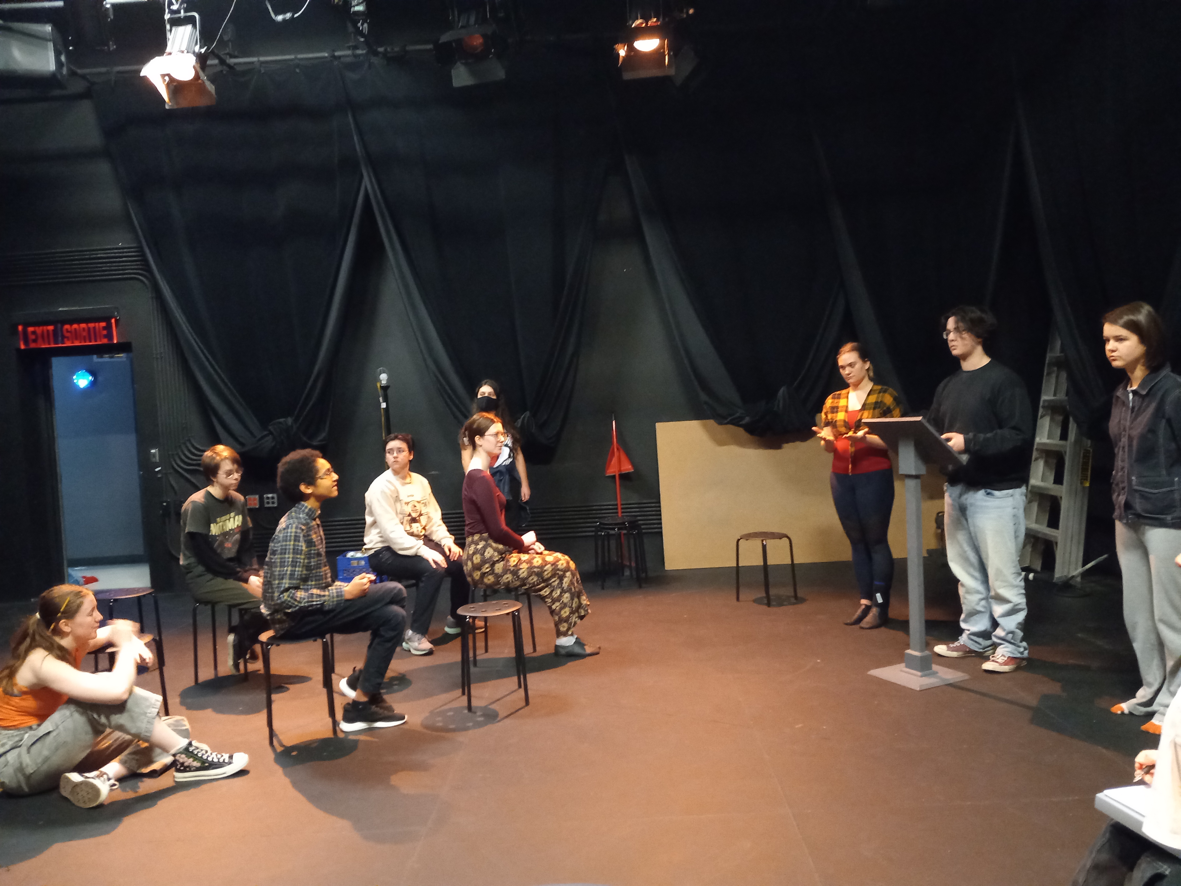 Youth sit on stools facing a podium