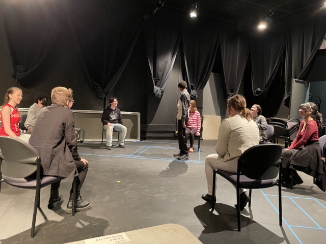 Youth sit in chairs and one stands
