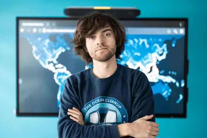 [Image Description: photo of young man in blue shirt with the ocean clean up logo and with loose short brown hair and facial hair.]