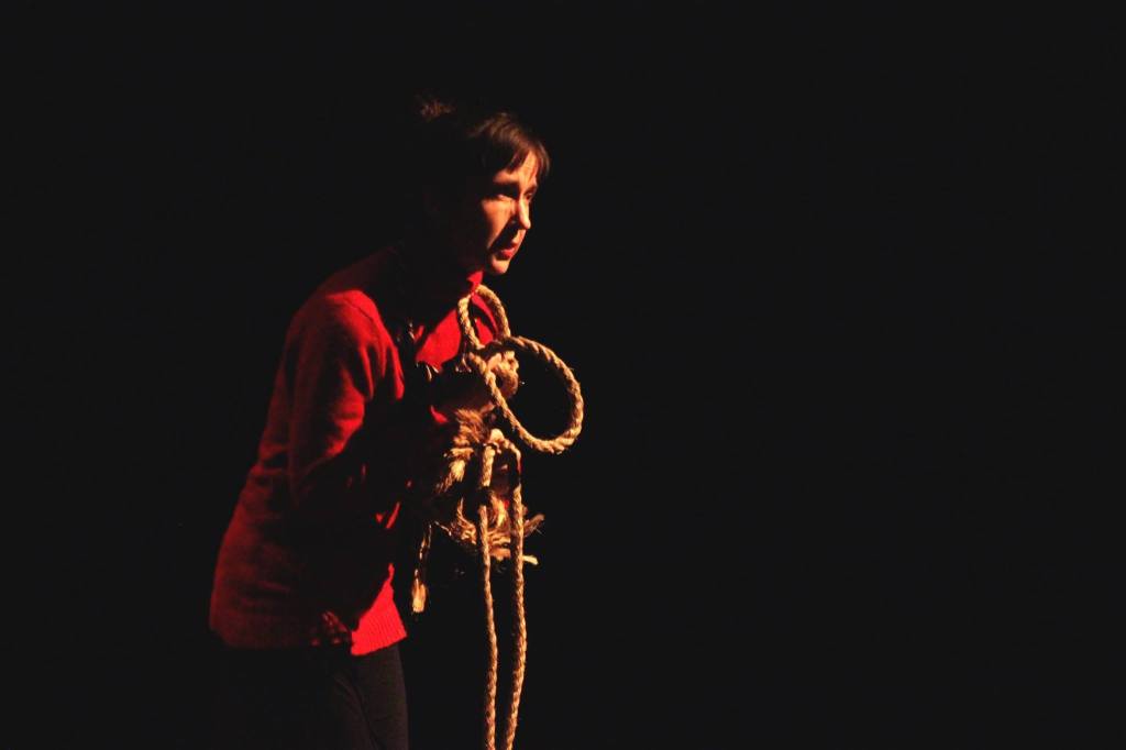 A woman wearing a red sweater clutches a rope and looks intently ahead