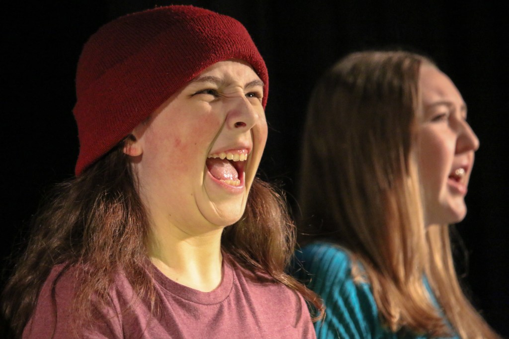 Two youth open their mouths wide and call out. One wears a red hat.