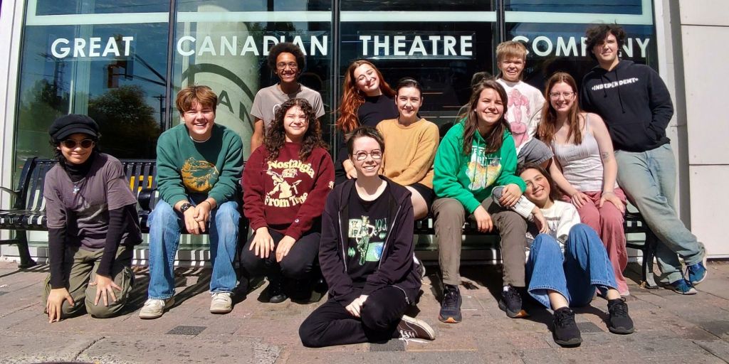 A group of youth in different coloured casula clothes sit and stand in from of a theatre window. Text: Great Canadian Theatre Company